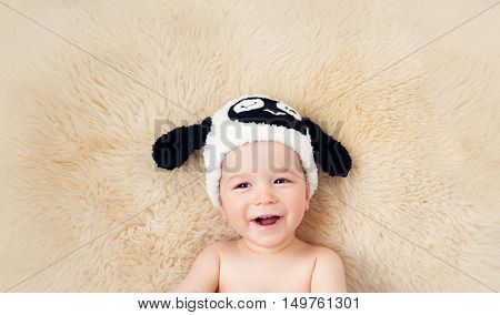 sleepy one year old baby lying in sheep hat on lamb wool background