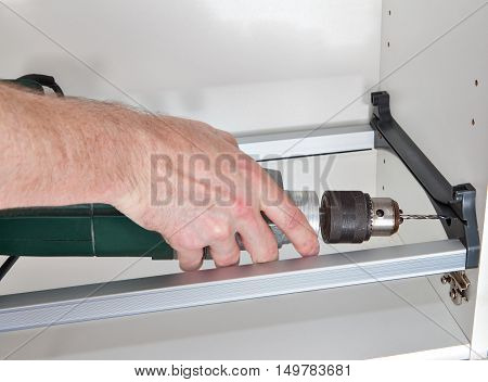 Installation of kitchen furniture build a wall cabinet for drying dishes woodworker hole is drilled using electric drill the workman hand holding power tools closeup.