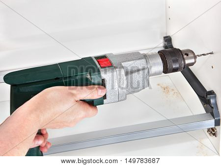 Assembly dish rack for drying dishes inside the kitchen cabinet man hand holding drilling tools carpenter hole is drilled using power drill.