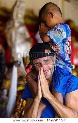 a pretty boy enjoying riding on man's back in a temple Phuket