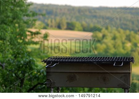 a empty portable BBQ grill in front of a fresh green summer landscape