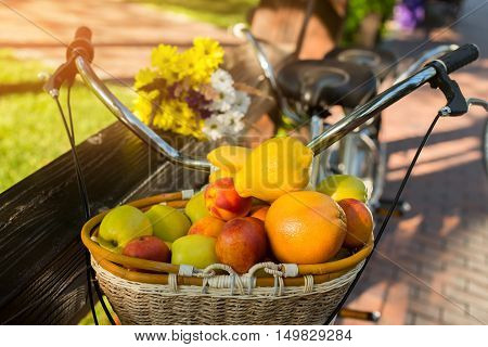 Basket filled with fruits. Bicycle near fence. Vitamins and energy of sun. Juicy apples and sweet peaches.