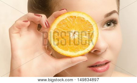 Young beautiful woman looking through a slice of orange in a kaleidoscope. Perfect skin. Grey background