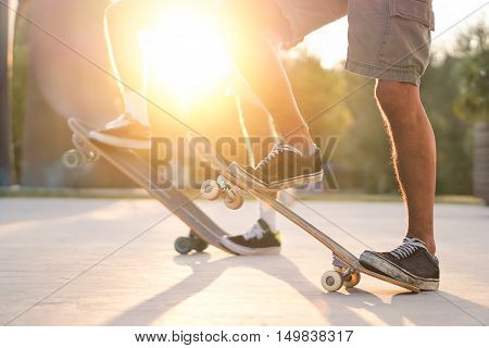 Closeup of two friends training with skateboard at sunset outdoors - Skaters standing on their longboards with back lighting - Extreme sport concept - Soft warm filter
