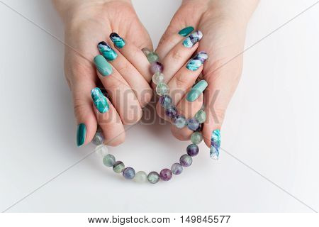 Closeup of woman nails with creative purple and green manicure. Fluorinit print. Natural stone beads. Copy space.