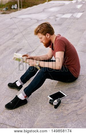 Tourist have relax time on lunch and explore the paper map. Man with camera and tablet sitting on stais. Opening city concept.