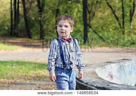 Smiling little boy with bow tie and jeans poses in sunny green park