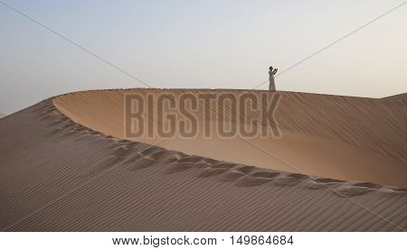 Man in traditional outfit praying in a desert at sunrise