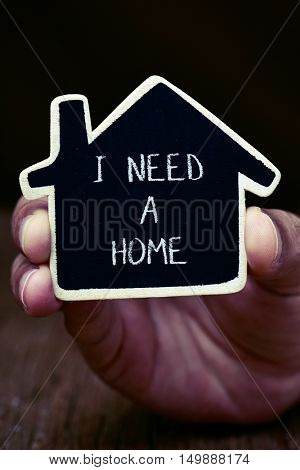 closeup of the hand of a young man showing a black house-shaped signboard with the text I need a home