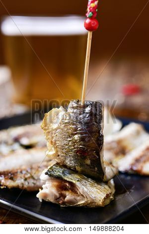 closeup of a plate with some spanish sardine fillets served as tapas, on a rustic wooden table, with a glass of refreshing beer in the background