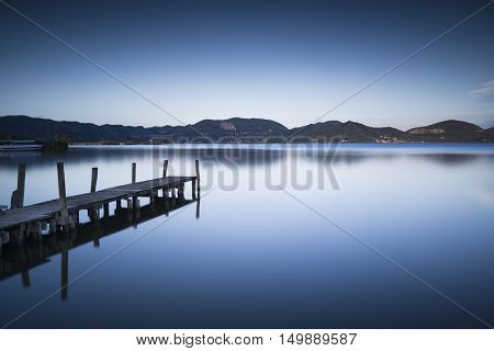 Wooden pier or jetty on blue lake sunset and sky reflection water. Long exposure Versilia Massaciuccoli Tuscany Italy.