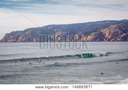 Seascape at Guincho beach and Cascais coastline, Portugal, with a group of surfers in the water.