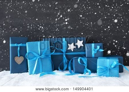 Blue Gifts Or Presents With Hearts And Stars. Black Cement Wall As Background With Snow And Snowflakes. Christmas Greeting Card For Seasons Greetings