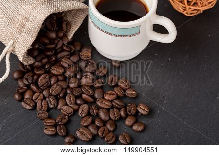 Heap coffe beans and cup of fresh coffee on dark background