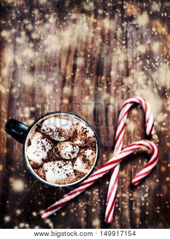 Cup of hot cocoa with marshmallows on wooden background. Christmas Card with decorations and falling snow