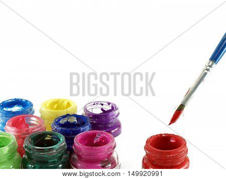 paintbrush dipped red colour and group of colorful opened glasses bottles of poster color isolated on white background, water soluble paint with art instrument for art work, close-up with copy space