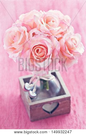 Artificial Pink Roses in a vase on a pink background.