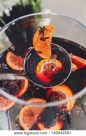 Making hot alcohol, mulled wine for sale at country fair. Glintwine from red wine with citrus and cloves in big glass, mixed with soup ladle. Closeup, vertical image