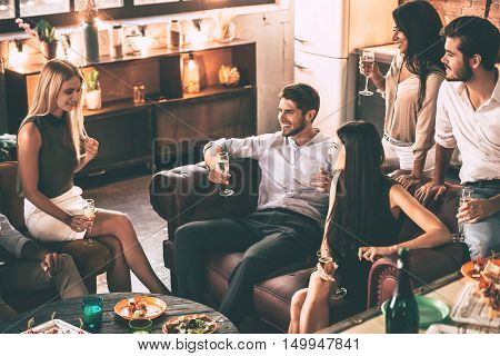 Carefree time with friends. Top view of cheerful young people enjoying food and drinks while spending nice time in cofortable chairs at home together