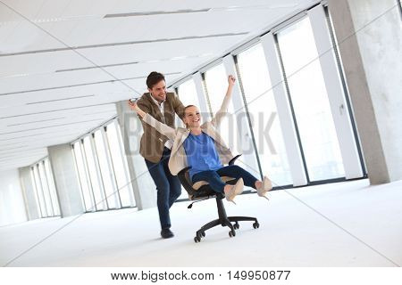 Full length of young businessman pushing female colleague in chair at empty office