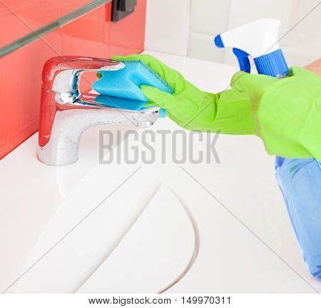 Woman cleaning sink and faucet in bathroom at home