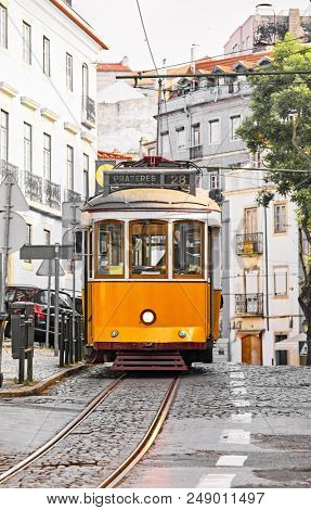 Lisbon, Portugal. Vintage yellow retro tram on narrow bystreet tramline in Alfama district of old town. Popular touristic attraction of Lisboa city.