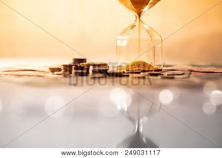 Reflection Of Brown Sand Running Through The Shape Of Modern Hourglass On Glowing Table With Currenc