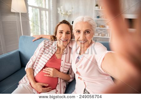 Striped Shirt. Pregnant Woman Wearing Striped Shirt Sitting On Sofa Near Her Old Friend Making Some 