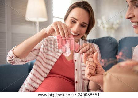 Cute Clothes. Beaming Pregnant Woman Smiling Broadly Feeling Happy While Looking At Clothes For Futu