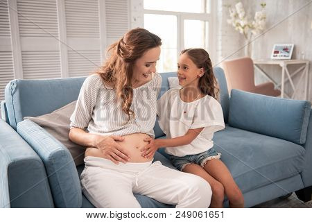Touching Belly. Excited Girl Wearing White Open Shoulder Blouse Touching Belly Of Her Pregnant Aunt