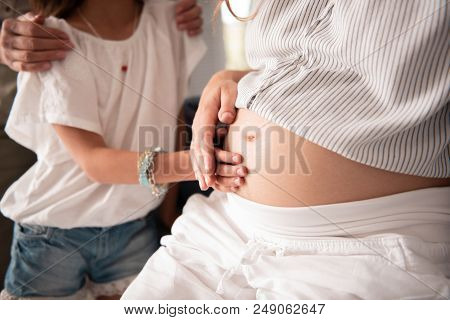 Stylish Bracelet. Little Caring Good-looking Daughter Wearing Stylish Bracelet Touching Pregnant Tum