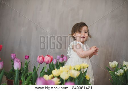 Beautiful Smiling Little Girl In White Lace Dress Among Tulips.