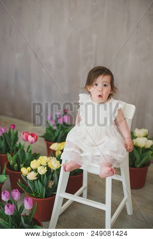 Beautiful Smiling Little Girl In White Lace Dress Among Tulips.