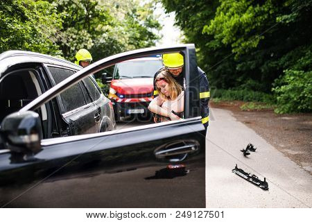 Two Firefighters Getting A Young Unconscious Woman Out Of The Car After An Accident.
