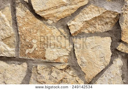 The Wall Is Made Of Beige Stones Of Various Shapes With Cement Seams.