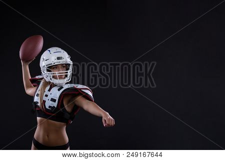 Sportive Serious Woman In Helmet Of Rugby Player Holding Ball In Stuio On Dark Background. Girl Spor