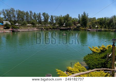 Green Clear Clear Mountain Lake In The Background Of A Park Zone With Tents And Umbrellas For Touris