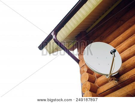 Satellite Dish On The Wall Of The House. Antenna Is White. The House Is Made Of A Wooden Beam Of Bro