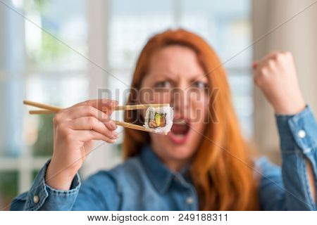 Redhead woman eating sushi using chopsticks annoyed and frustrated shouting with anger, crazy and yelling with raised hand, anger concept