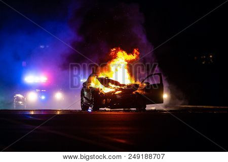 Car On Fire At Night With Police Lights In Background