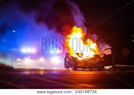 Car On Fire At Night With Police Lights In Background
