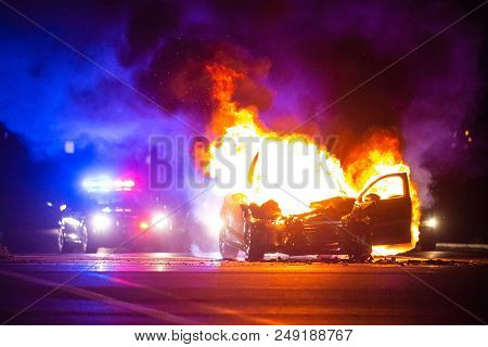 Car On Fire At Night With Police Lights In Background