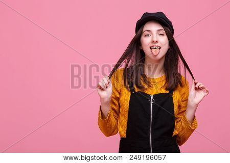 A Girl Dressed In Warm Yellow Sweater And Black Autun Overalls Is Playing With Her Hair And Showing 