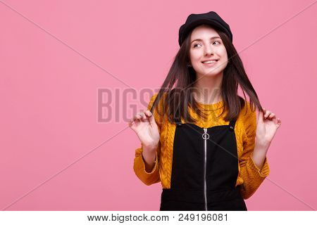 A Girl Dressed In Warm Yellow Sweater And Black Autun Overalls Is Playing With Her Straight Hair.