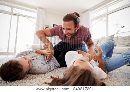Father Tickling Children As They Play Game In Lounge Together