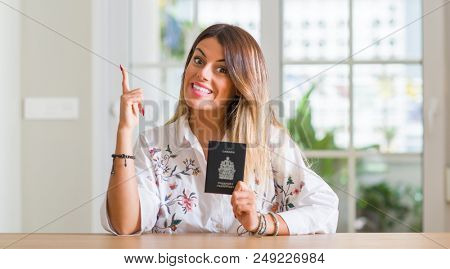 Young woman at home holding a passport of Canada surprised with an idea or question pointing finger with happy face, number one