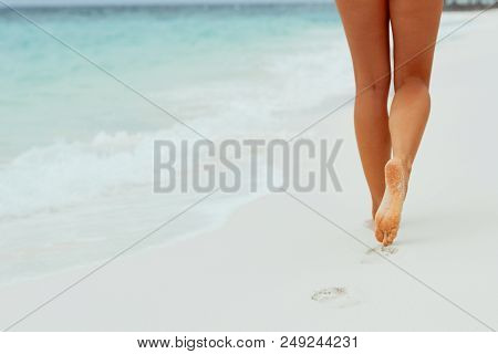 Woman Walking On Sand Beach Leaving Footprints In The Sand. Close Up Of Woman Leg On The Beach. Feet