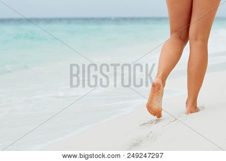 Woman Legs And Feet Walking On The Sand Of The Beach With The Sea Water In The Background. Foot Fema
