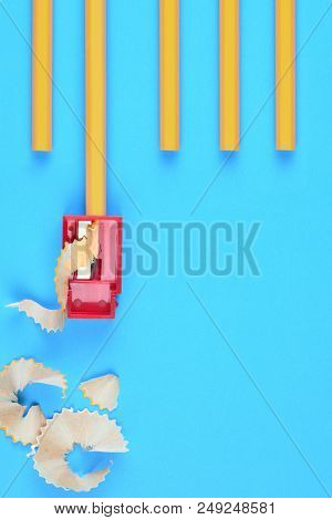 Back to School Concept: Unsharpened Yellow Pencils with a sharpener and shavings, on a blue background. Copy space on the lower right side.