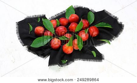 Bunch Of Red Sweet Plums With Green Leaves On A Black Towel On A Light Background. Top View, Space F